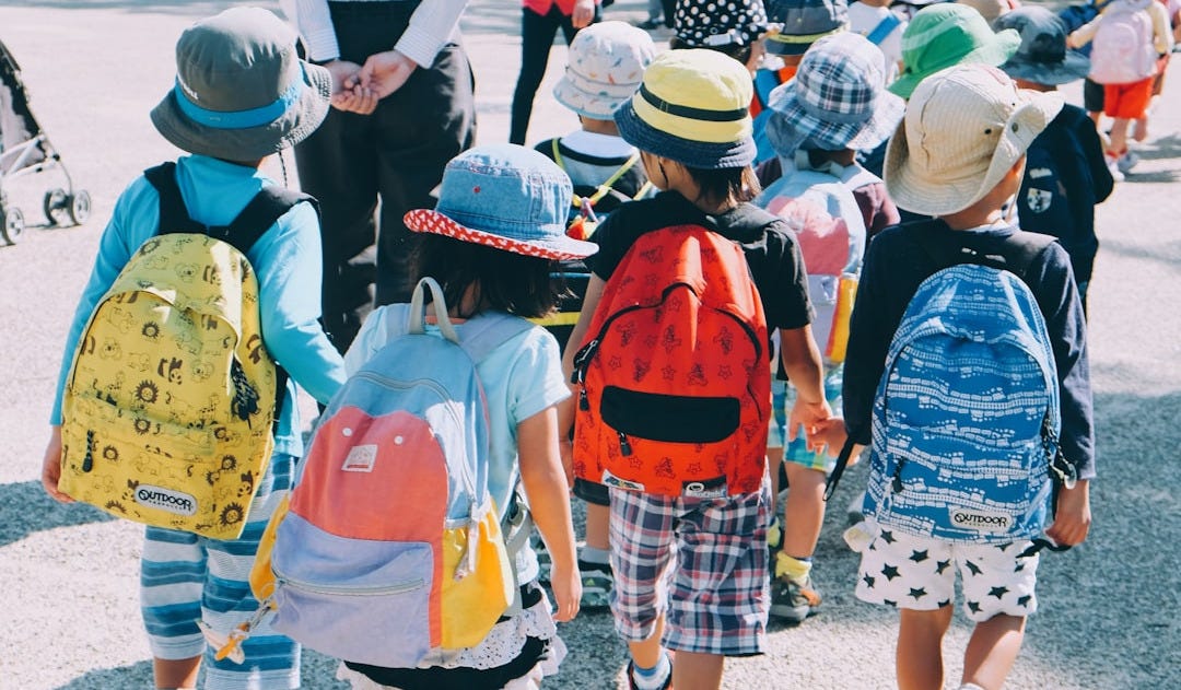 group of people wearing white and orange backpacks walking on gray concrete pavement during daytime