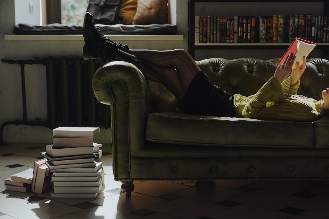 Free Person Lying Down on Sofa Reading a Book Stock Photo