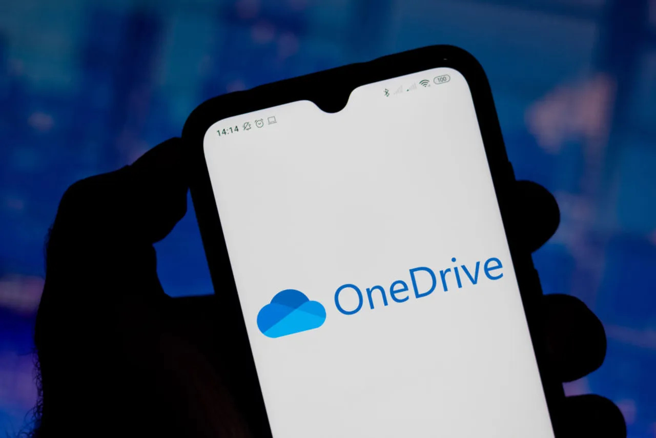 Silhueta de uma mao segurando um celular com o logo do One Drive