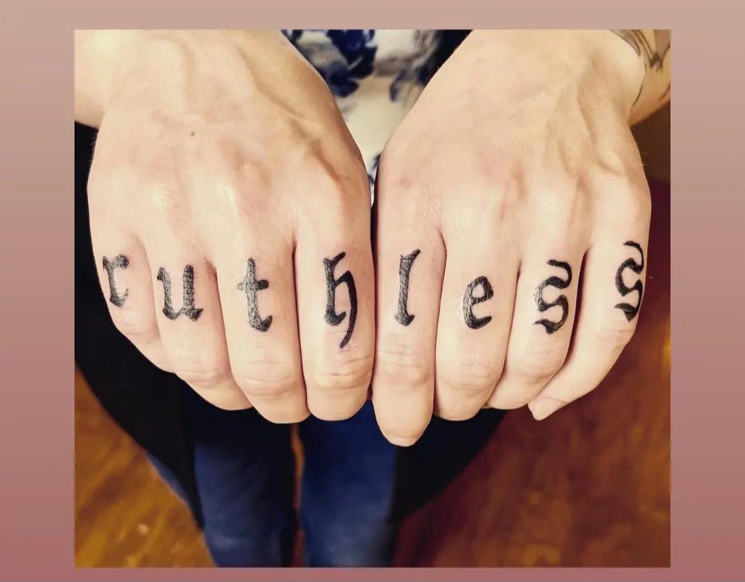 A close-up photo of Sarah's hands, right after getting the word, "ruthless," tattooed across her knuckles, in black, slightly ornate font.