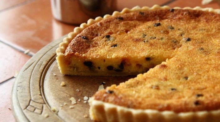 A golden brown Yorkshire Curd Tart studded with raisins on a wooden round board with a slice cut out