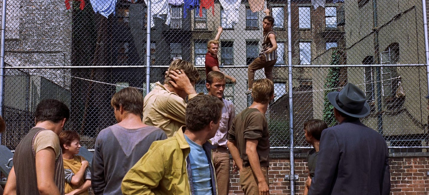 The Jets gang mooch around in a playground in 1961 movie West Side Story. Some hang from a chain-link fence like monkeys. A plain-clothes police officer in a suit and a fedora observes