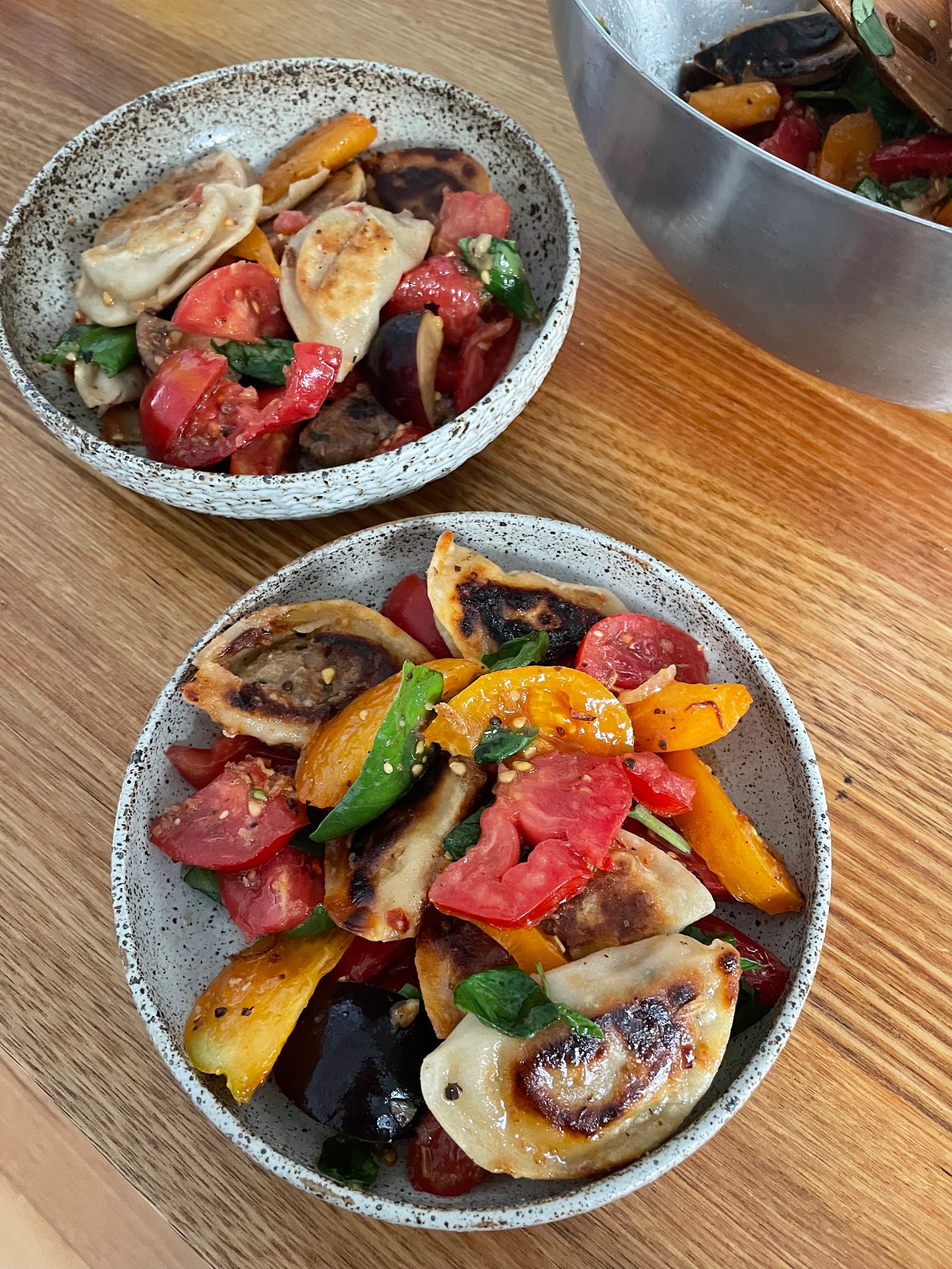 Two bowls of colourful dumpling salad, with panfried dumplings and heirloom tomatoes and basil