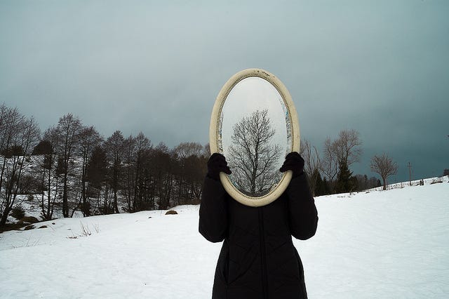 winter mirror, winter self reflection, woman holding a mirror in front of her face on a snowy day