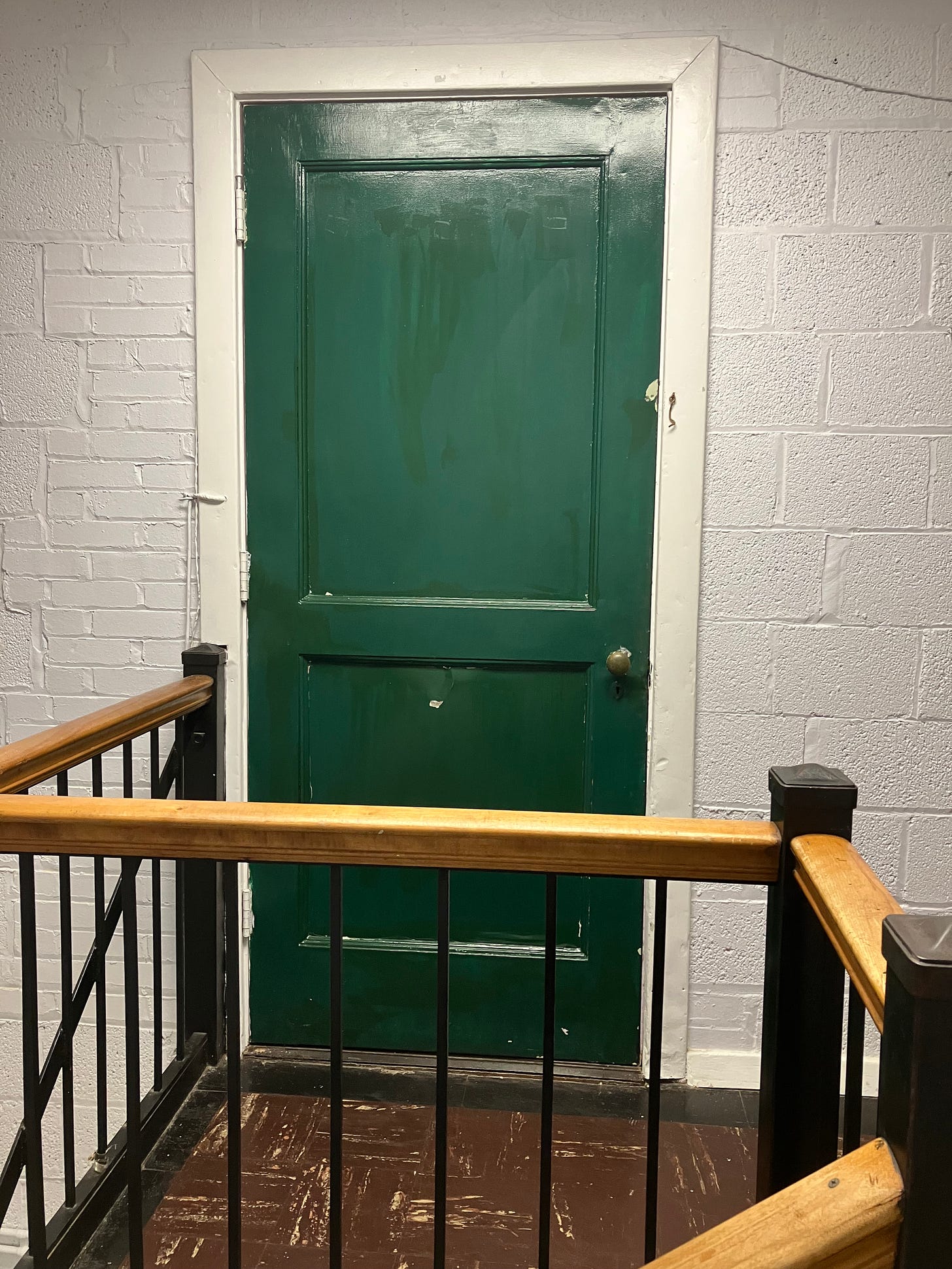 A photograph of a door situated at the top of a staircase inside Flowerbomb's practice space. The door is painted an emerald shade of green.