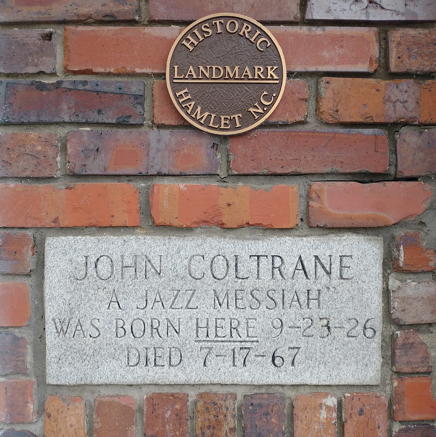 Historical marker on brick building reading "John Coltrane, A Jazz Messiah, was born here 9-23-26 died 7-17-67