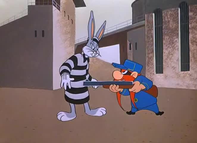 Still from the cartoon Looney Tunes. One character named Yosemite Sam holds another character, Bugs Bunny, at gunpoint. Bugs is dressed as a prisoner and Sam as a guard.  