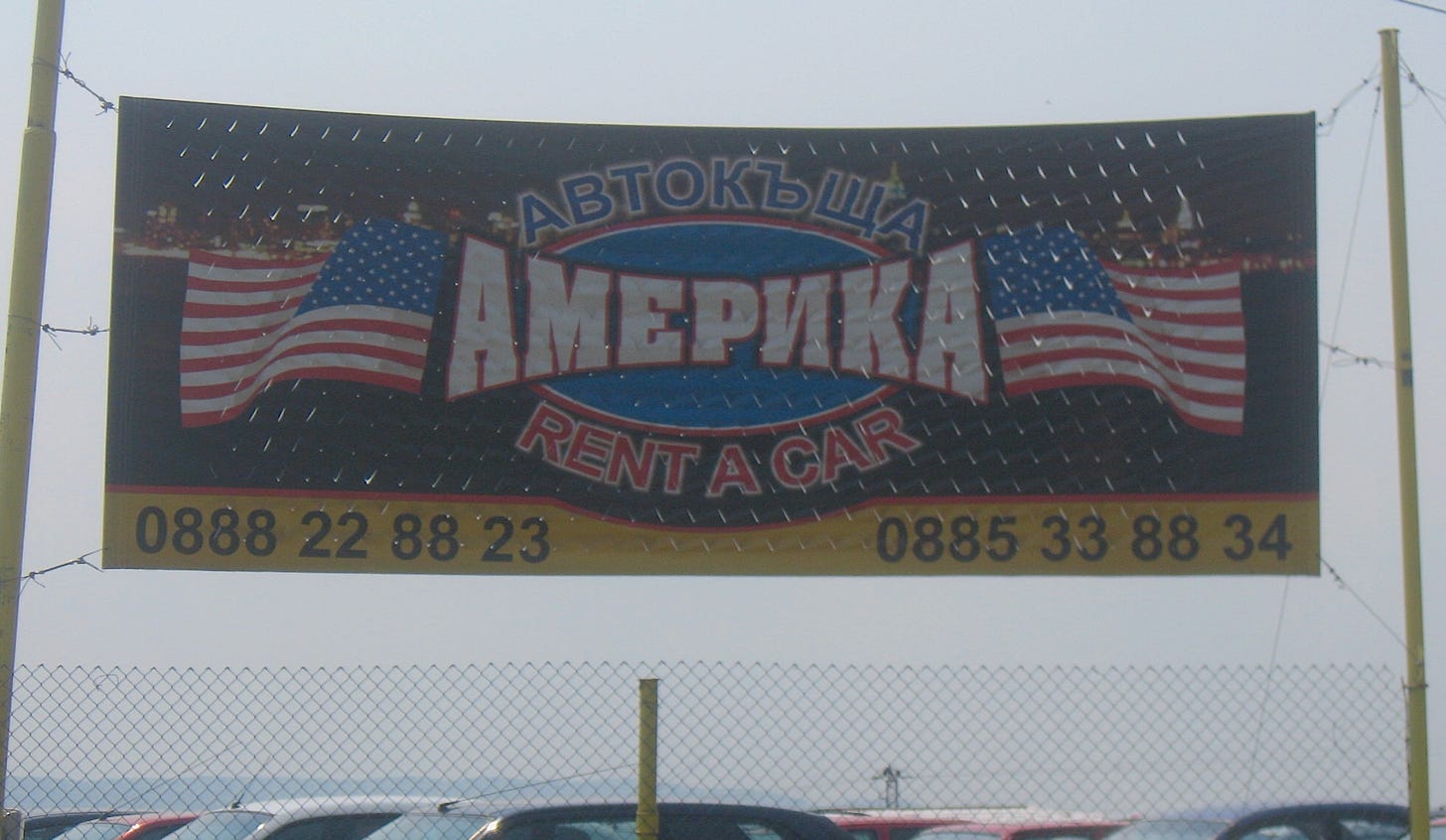 A sign above a parking lot reads "AMERICA Rent a Car" in both Bulgarian and English