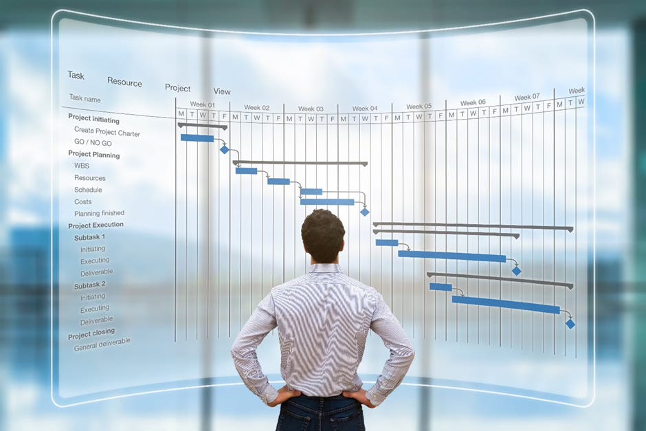 The image shows a man looking at a transparent screen displaying a detailed project management Gantt chart. The chart provides a visual timeline and breakdown of various tasks, resources, and project execution phases. The man appears to be carefully examining the information on the screen, likely using this project management tool to plan, monitor, and manage the progress of the project.