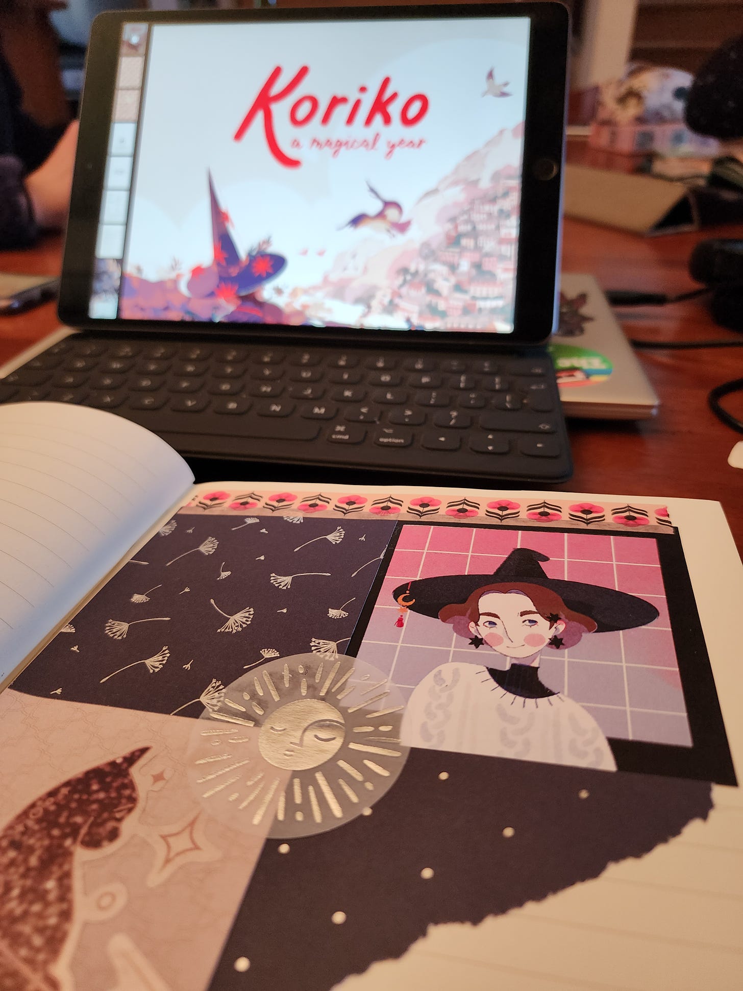 A scrapbook page that shows a drawing of a young witch and other interesting paper surrounding him. In the background, the digital version of Koriko sits open on an iPad.