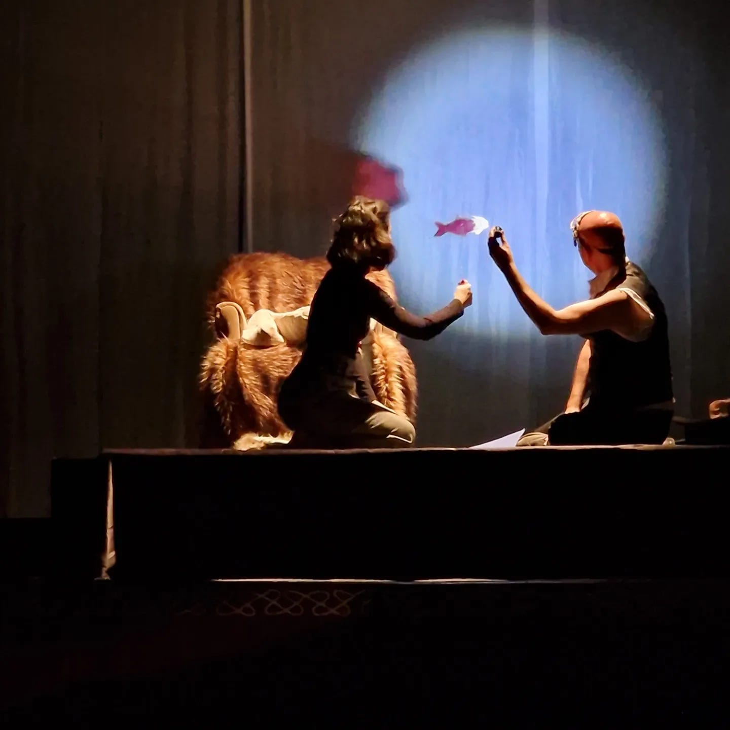 an actress and actor on their knees with a fish stick puppet in a spotlight. 