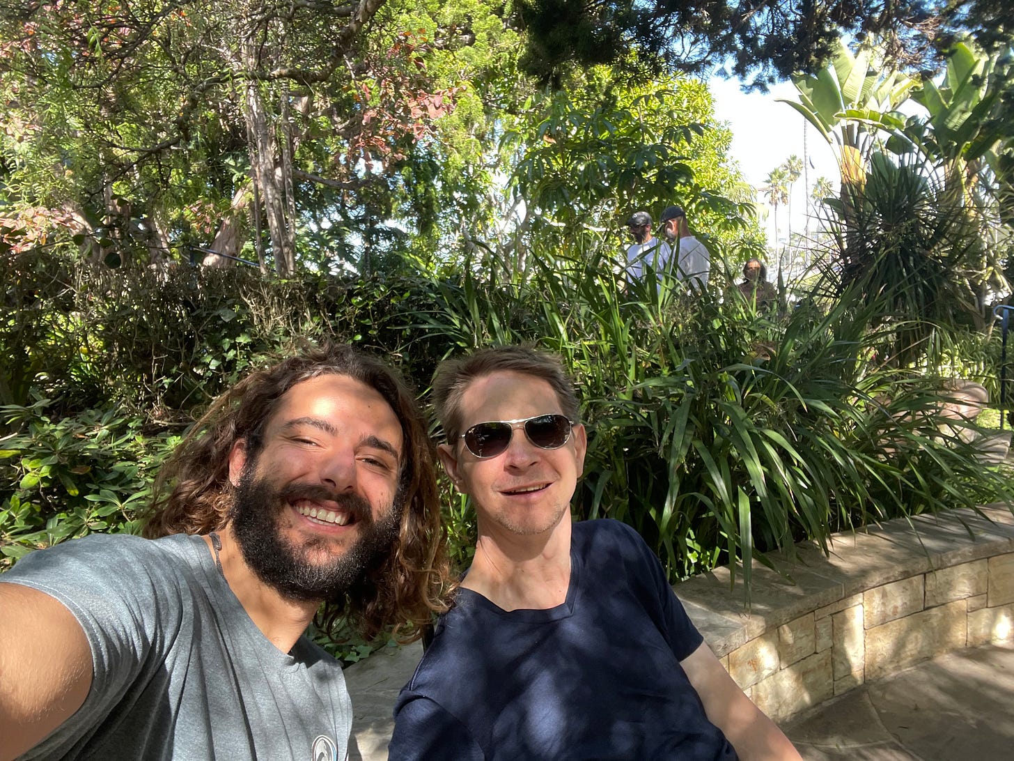 Kabir and Zach selfie with beautiful foliage of the meditation garden in the background. Speckled sunlight throughout.