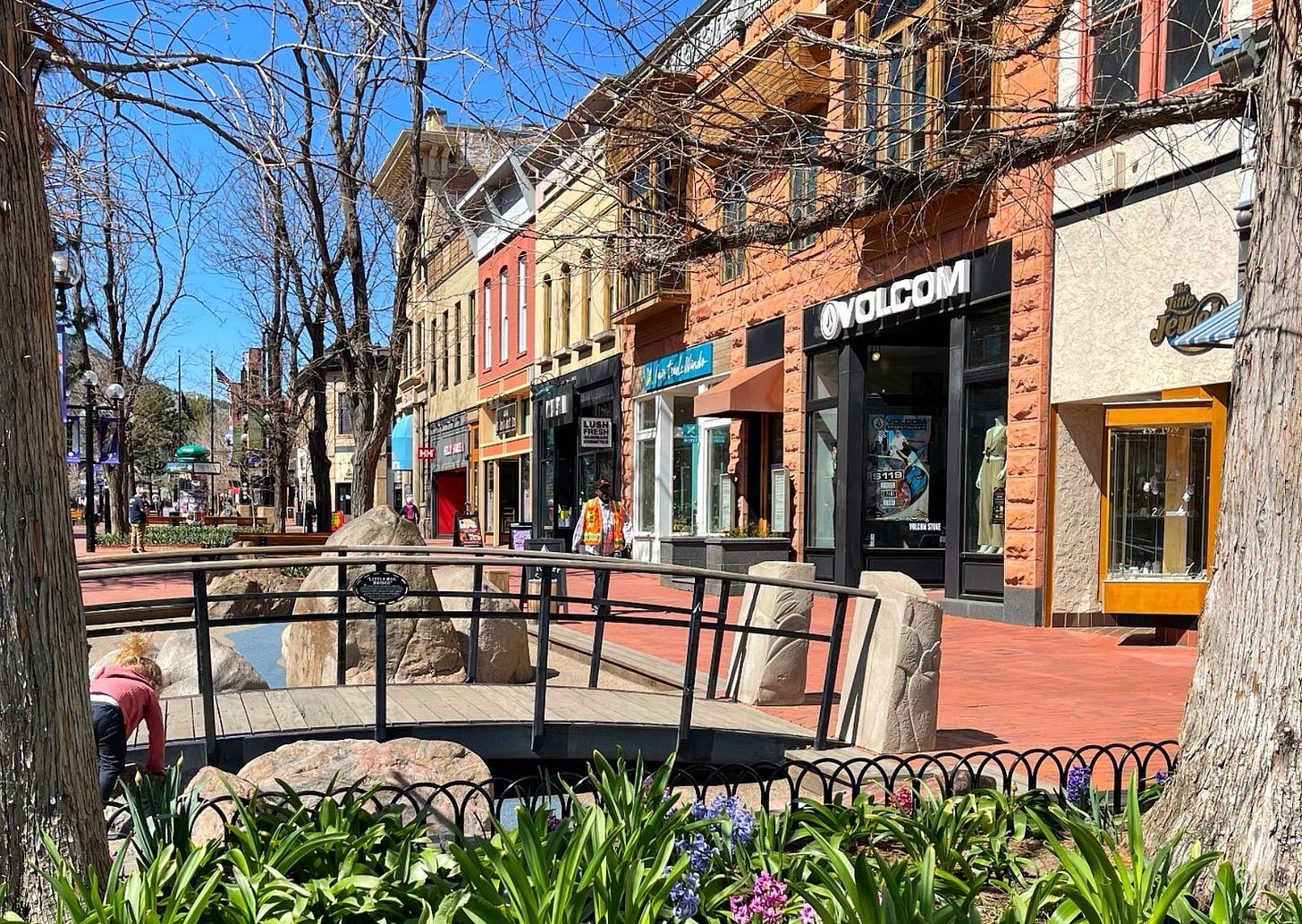 pearl street in Boulder, Colorado, a pedestrian area with green, playgrounds, and boutique shops and cafes against a blue sky
