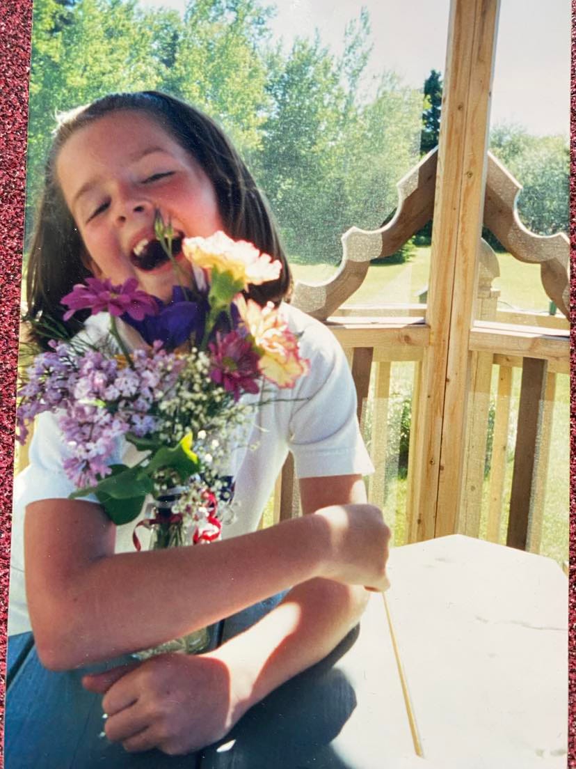 a photo of young me, missing a tooth, and hugging a vase of flowers.