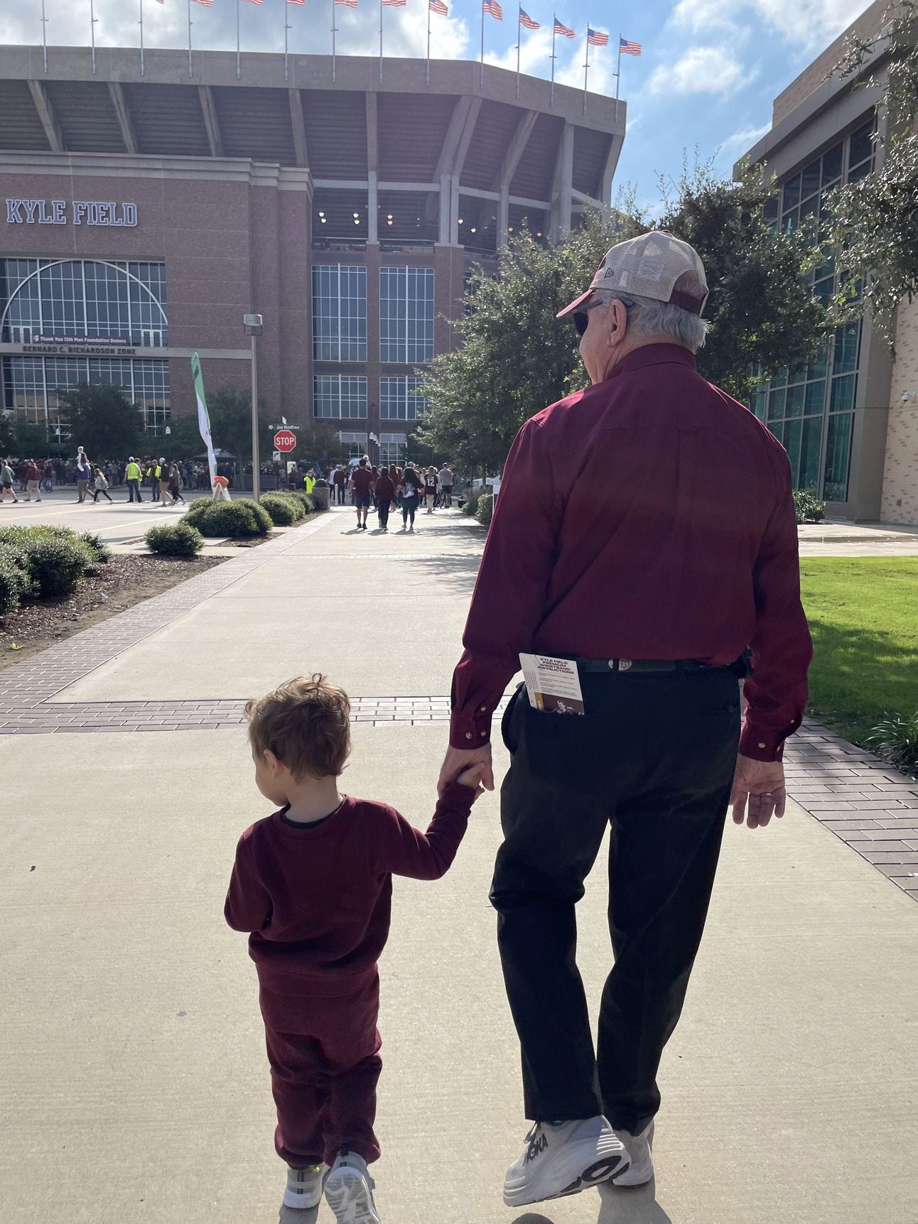 A young child and his great-grandfather walkin hand in hand to a football stadium A young child and his great-grandfather walkin hand in hand to a football stadium