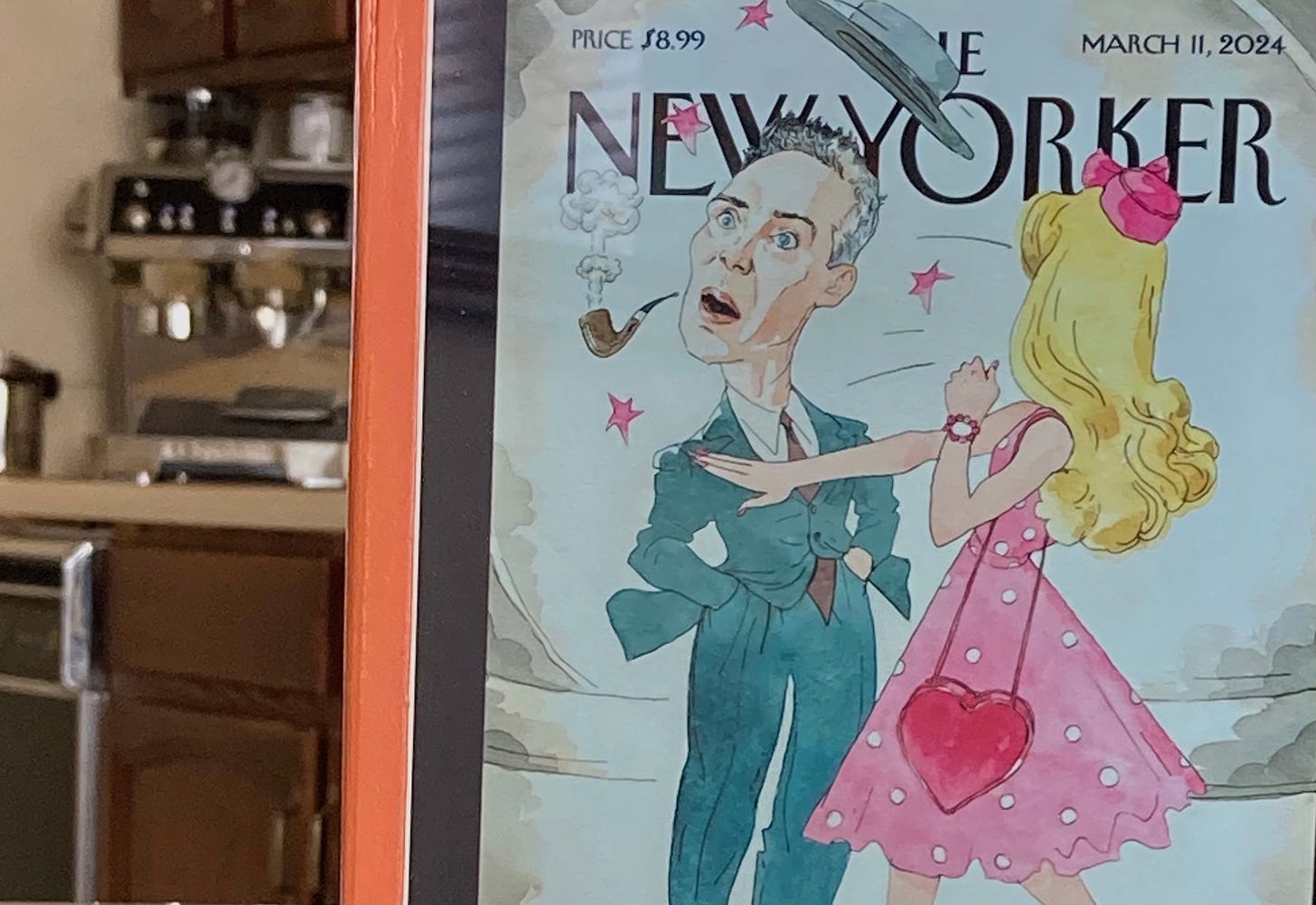 Author photo of iPad at kitchen table showing image of The New Yorker magazine's "Slappenheimer" cover, showing cartoon Barbie slapping Oppenheimer, knocking his pipe from his mouth and sending his hat flying off his head.