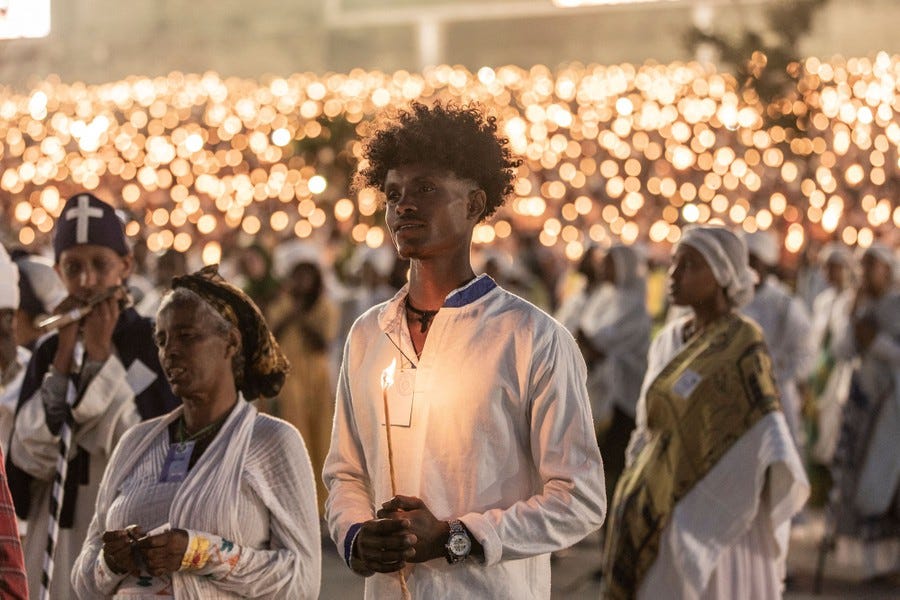 Hundreds of people dressed in white stand together holding lit candles.