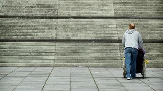 Man with a wheelchair at the bottom of a large staircase