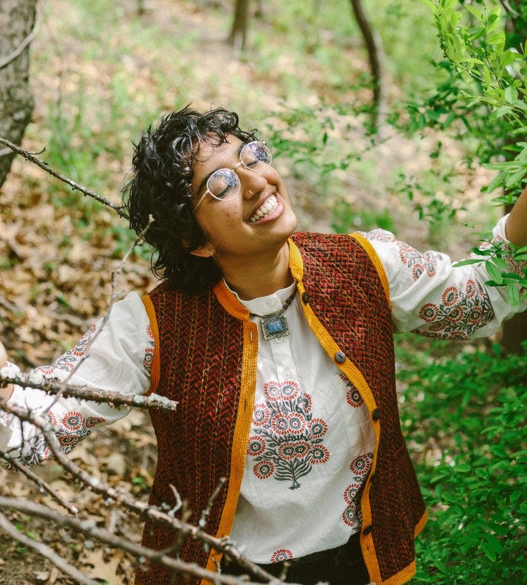 Anju in a forest smiling with their eyes closed