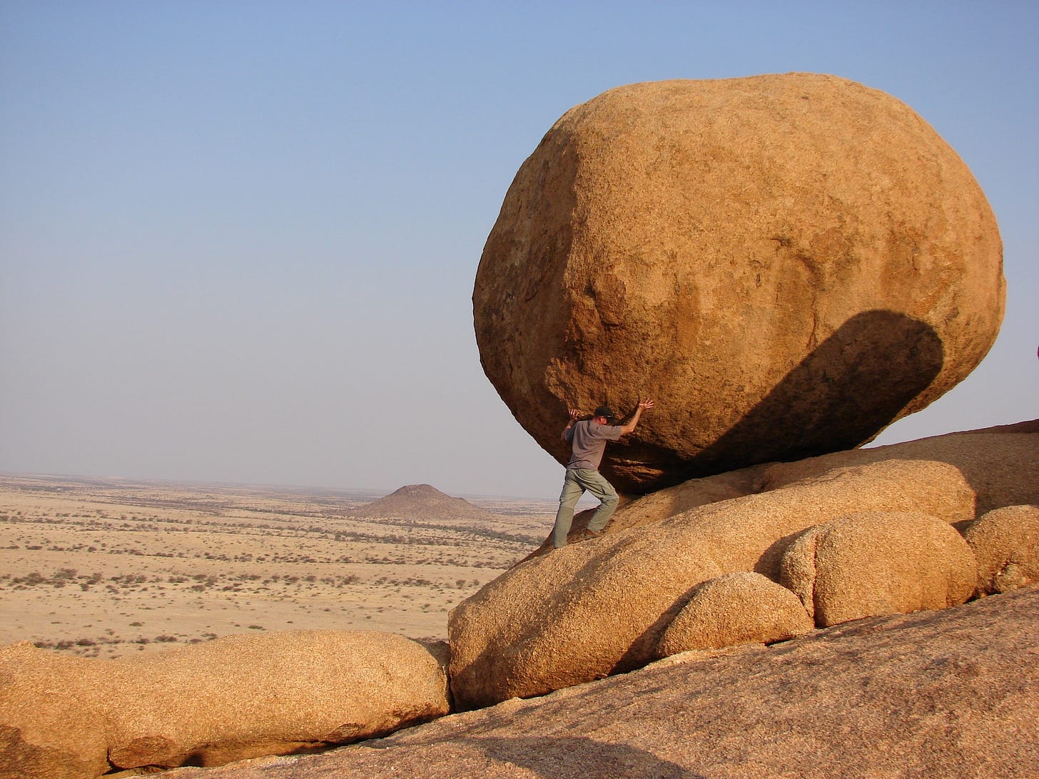 Man in the desert trying to move a massive rock 50 times bigger than him