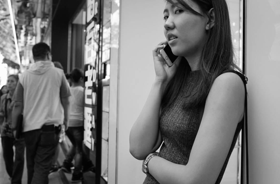 A woman on the phone leans against the wall on a busy street