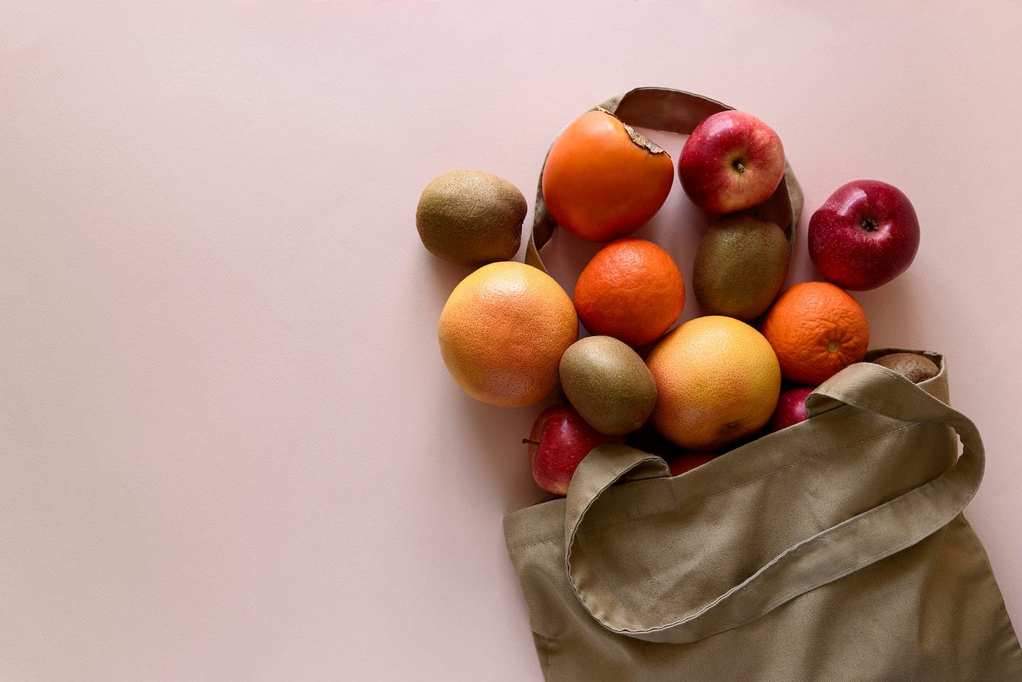Photo of various fruits spilling from a canvas bag onto a table