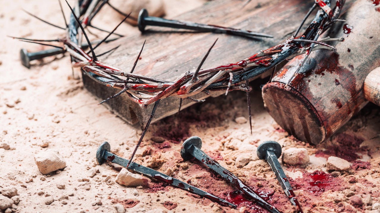 A bloody crown of thorns next to bloody nails and a hammer.