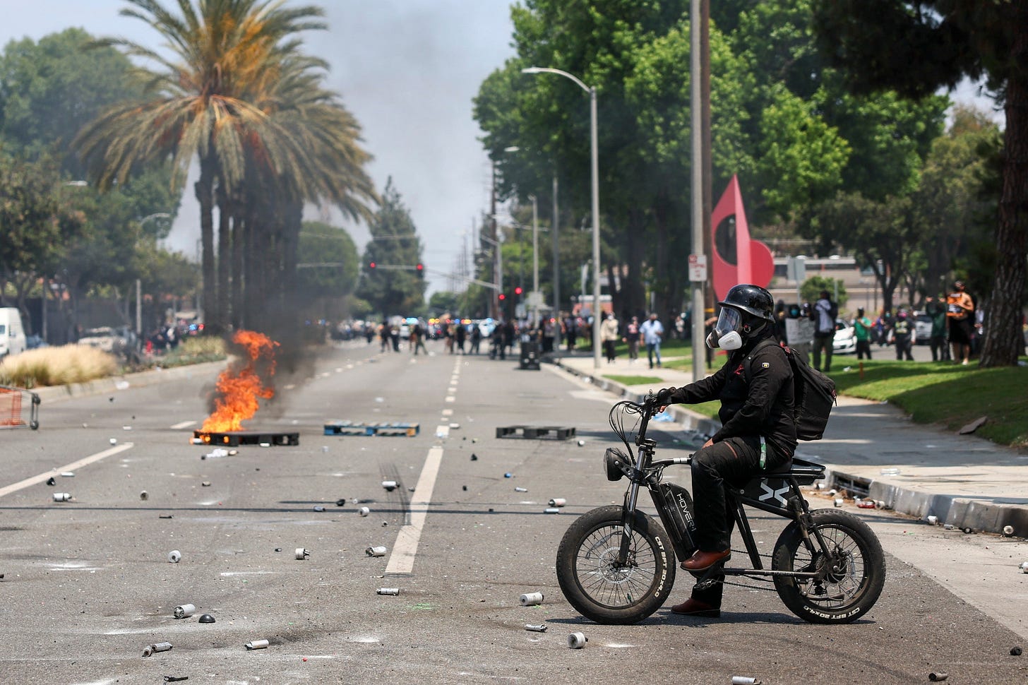 A protester sits on a bike as a crate burns in the street A protester sits on a bike as a crate burns in the street