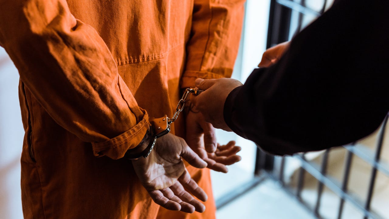 A person wearing an orange jumpsuit being put in handcuffs.