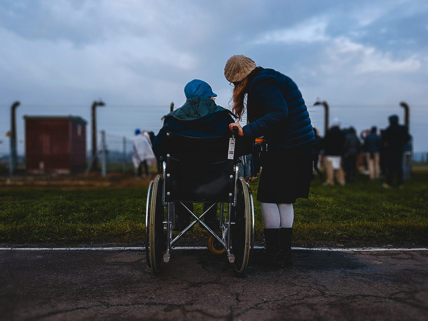 A Holocaust survivor in a wheelchair with a woman standing. They are watching Jewish youth playing in the death camp Auschwitz,