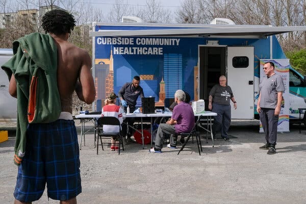 People sit at a table outside a mobile health clinic. 