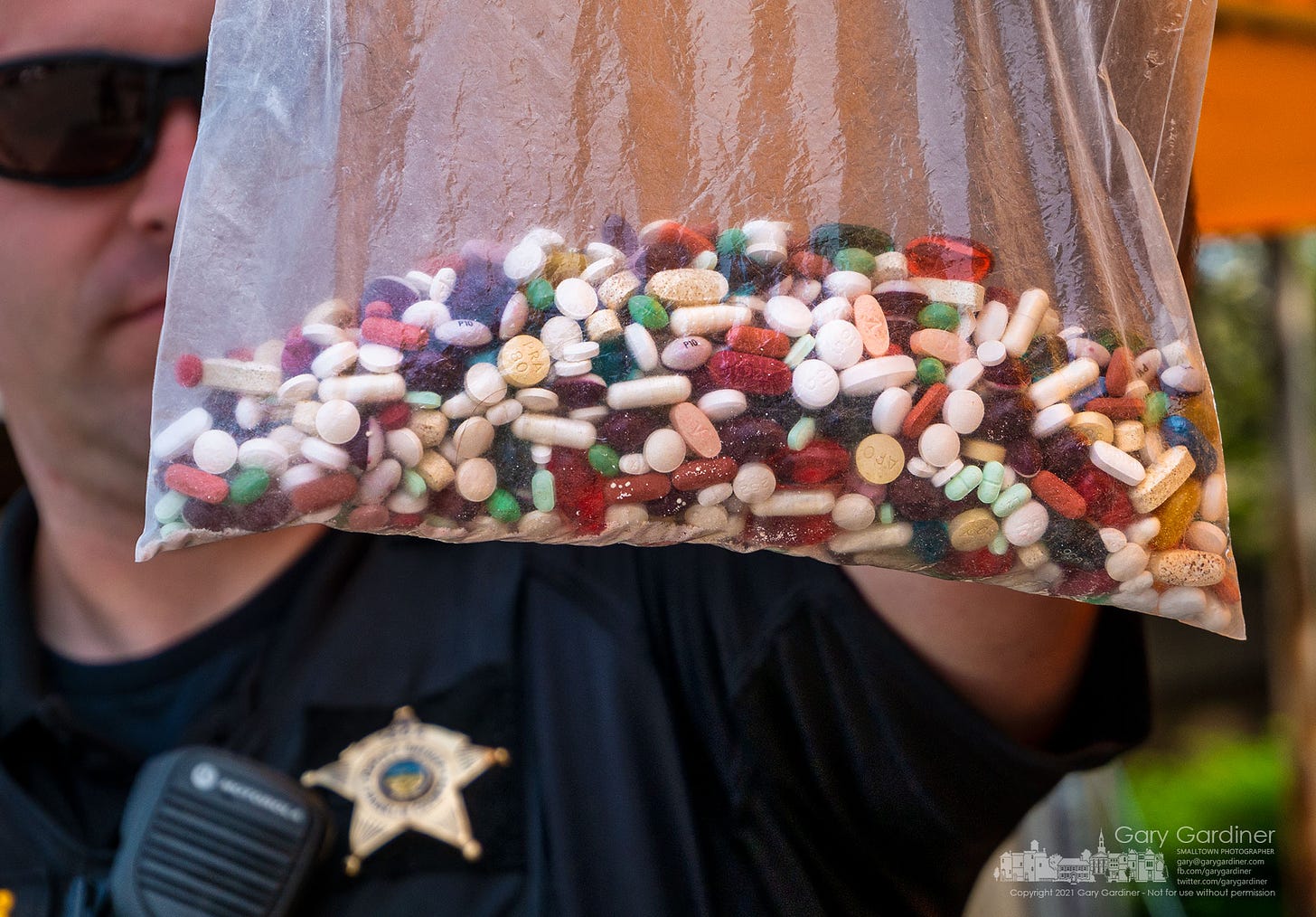 A Franklin County Deputy Sheriff holds a plastic bag containing unused, expired, or not needed prescription and over-the-counter drugs dropped off in the drive-thru at the Kroger on Schrock Road during Saturday's event sponsored by the Ohio Attorney General. My Final Photo for July 31, 2021.