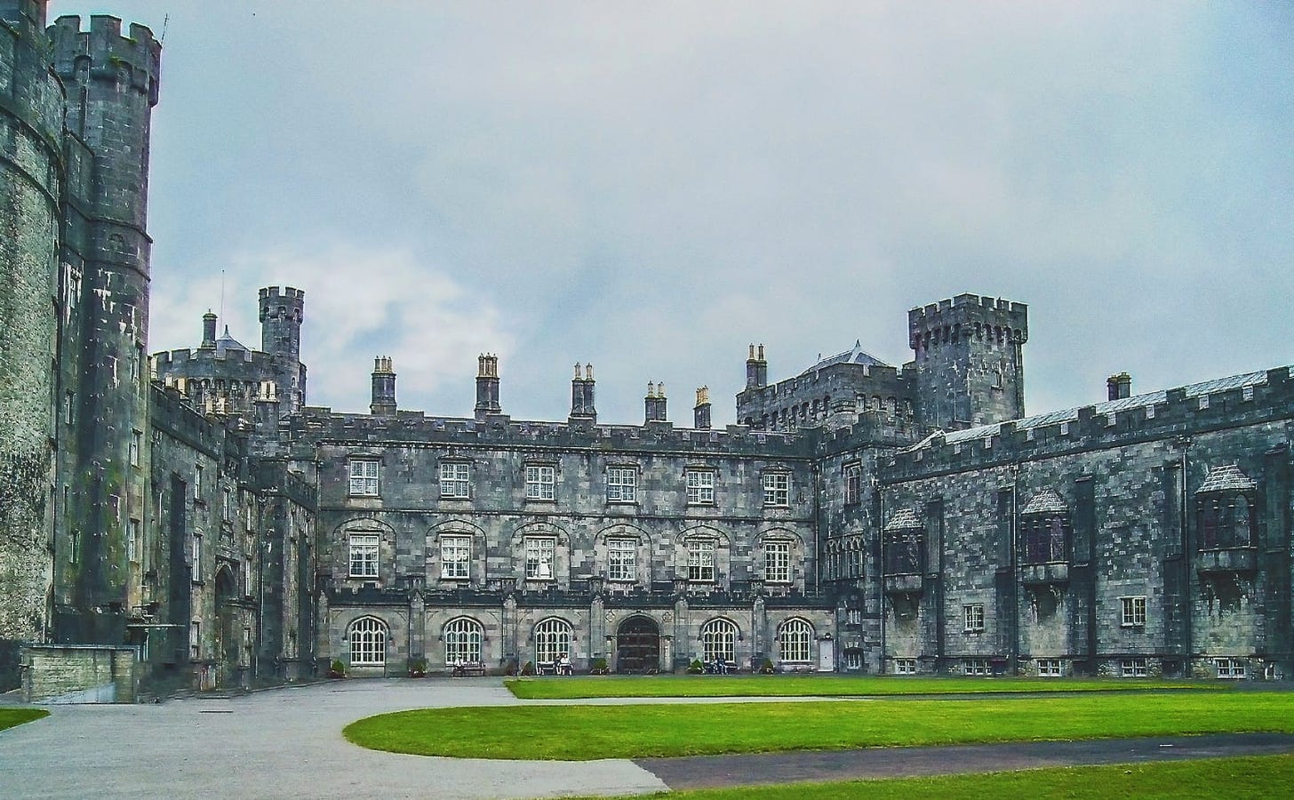 gray stone castle with green grassy lawns in the foreground and a pale blue sky overhead