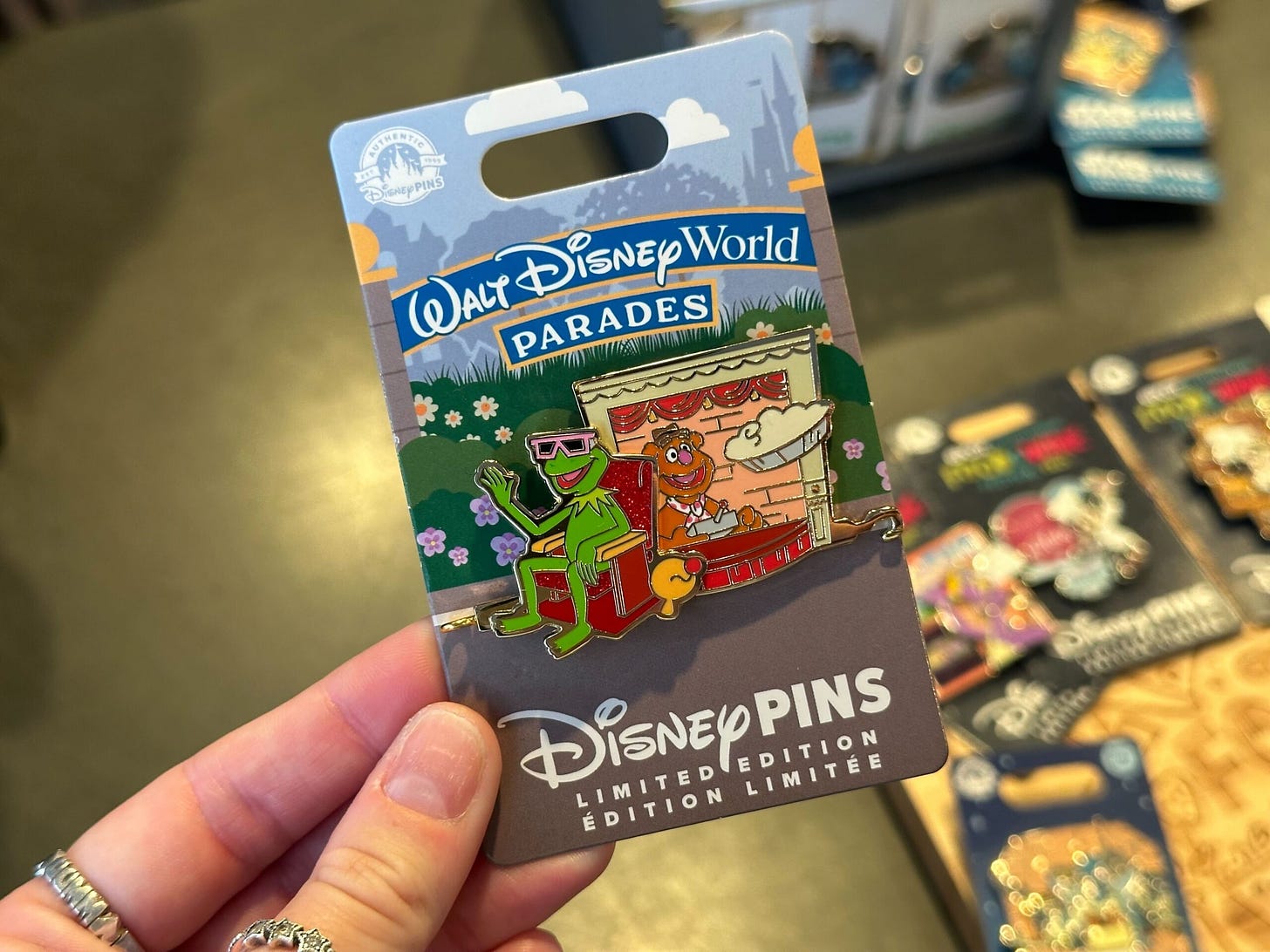 Hand holding a limited edition Walt Disney World Parades pin featuring a frog wearing sunglasses on a float.