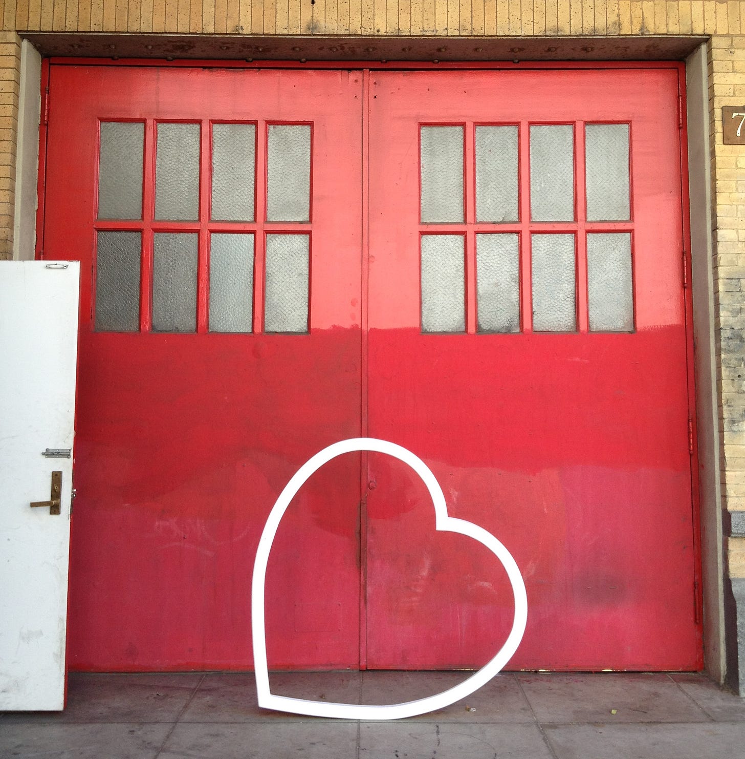 A photo of a giant white heart in front of red doors.