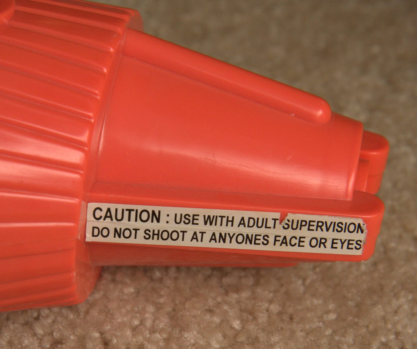 A bright orange cap with a sticker on it that says "Caution: use with adult supervision do not shoot at anyones face or eyes"