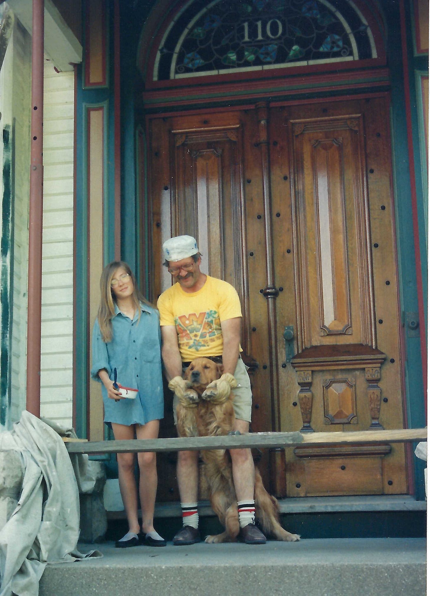 Two people standing in front of large walnut double doors with ornate details. A crescent-shaped stained glass window is above the doors.