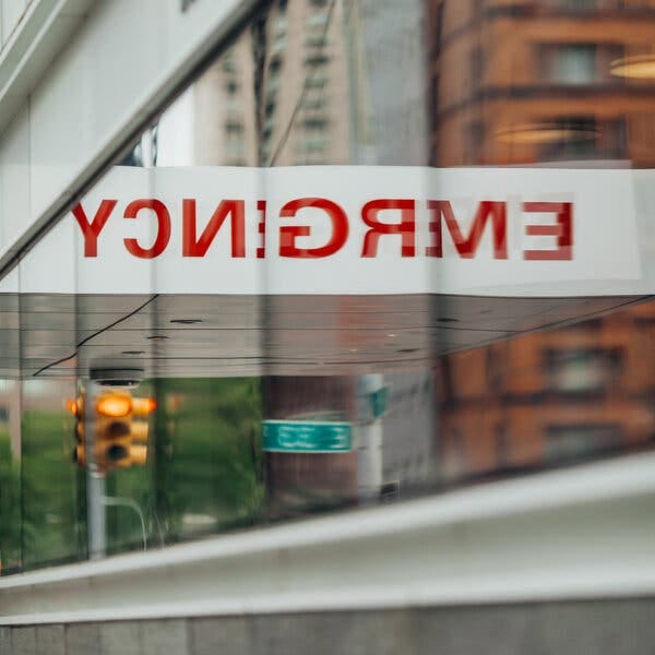 A hospital’s emergency entrance reflected in the windows on the street.