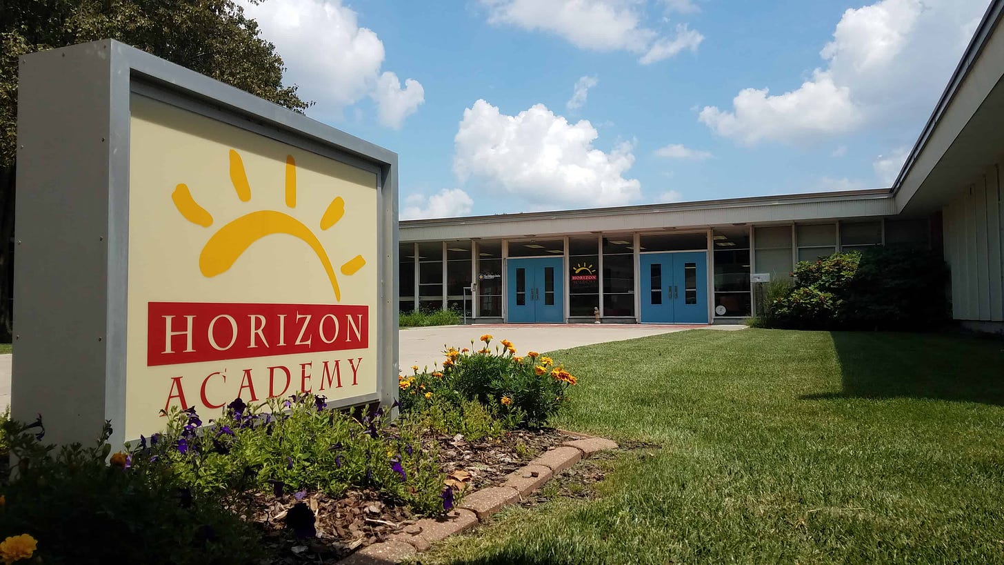 Picture of a school with two blue entry doors in the background and a prominent sign reading Horizon Academy.