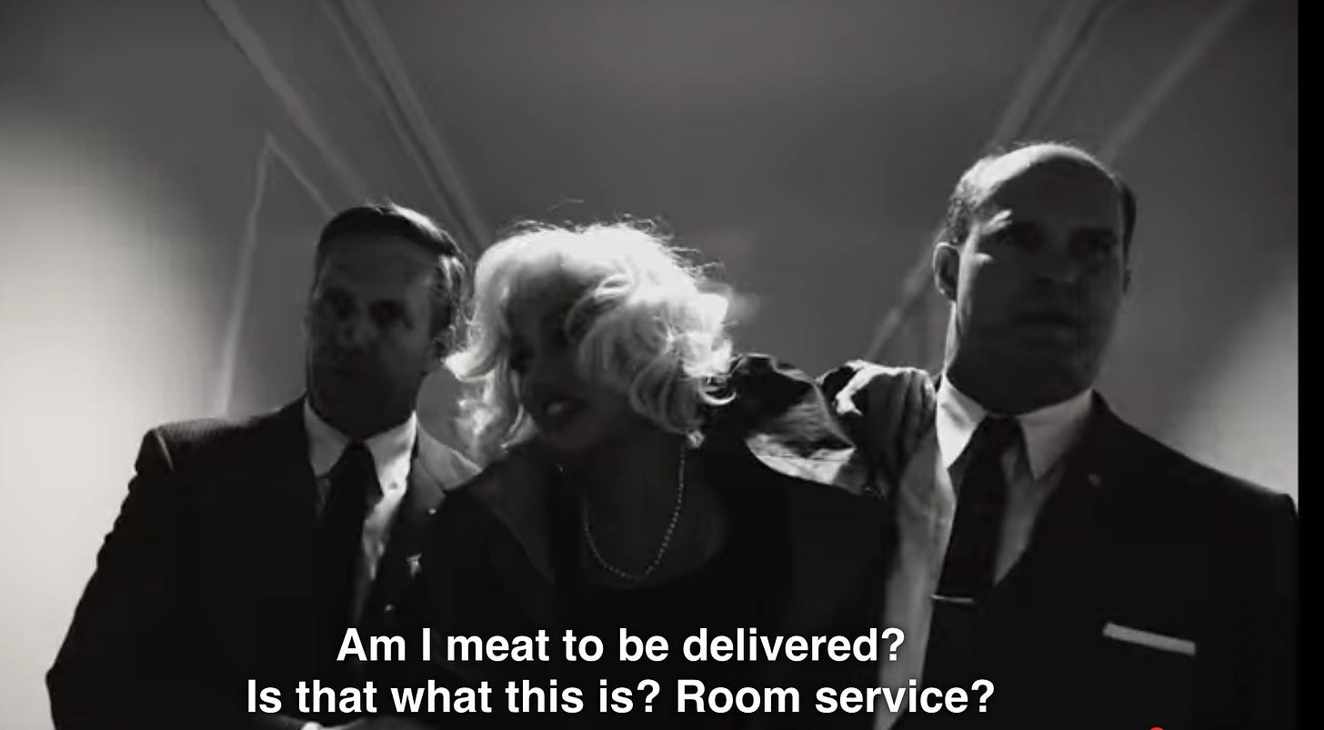 Marilyn Monroe is carried between two men in black suits down a hotel hallway.