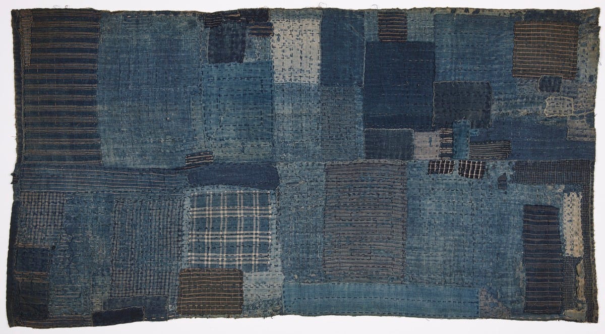 A textile made up of many rectangular patches of indigo-dyed fabric, sewn together in a mosaic-like pattern. The patches vary in shades of blue and include different textures and patterns such as stripes, plaids, and solids, with visible stitching throughout. A textile made up of many rectangular patches of indigo-dyed fabric, sewn together in a mosaic-like pattern. The patches vary in shades of blue and include different textures and patterns such as stripes, plaids, and solids, with visible stitching throughout.
