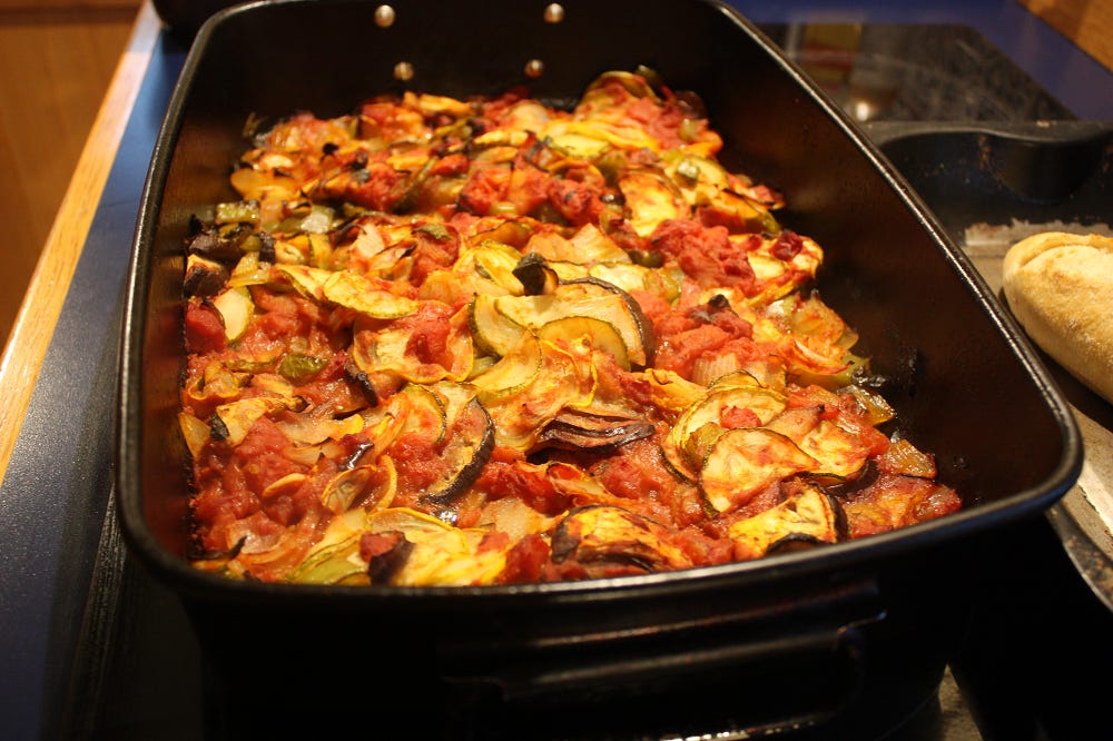 A roasting tin full of tomatoey-roasted veg, and a glimpse of crusty bread halfway out of shot. Mm.
