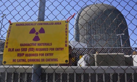 a yellow sign on a chain link fence in front of a grey power plant