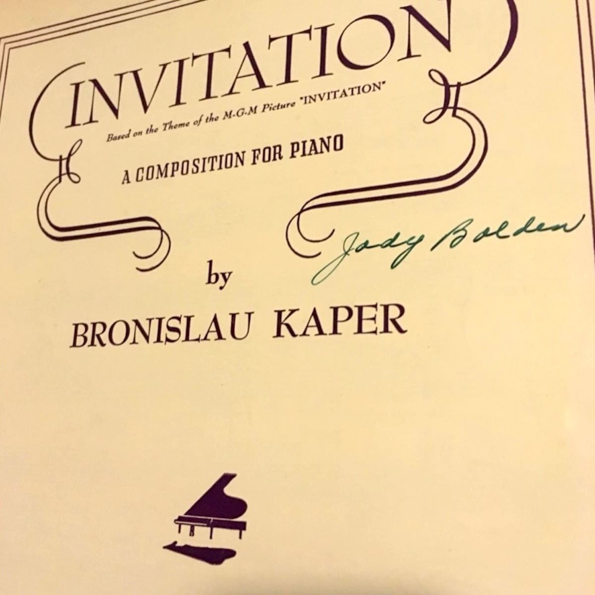 Sheet music cover has a lined border and ornate trim around the title with a small illustration of a piano floating off an invisible ground, all in dark purple print. It reads: INVITATION. Based on the Theme of the M-G-M Picture *INVITATION*. A COMPOSITION FOR PIANO by BRONISLAU KAPER. Jody Bolden’s signature is in green ink to the right side under the title.