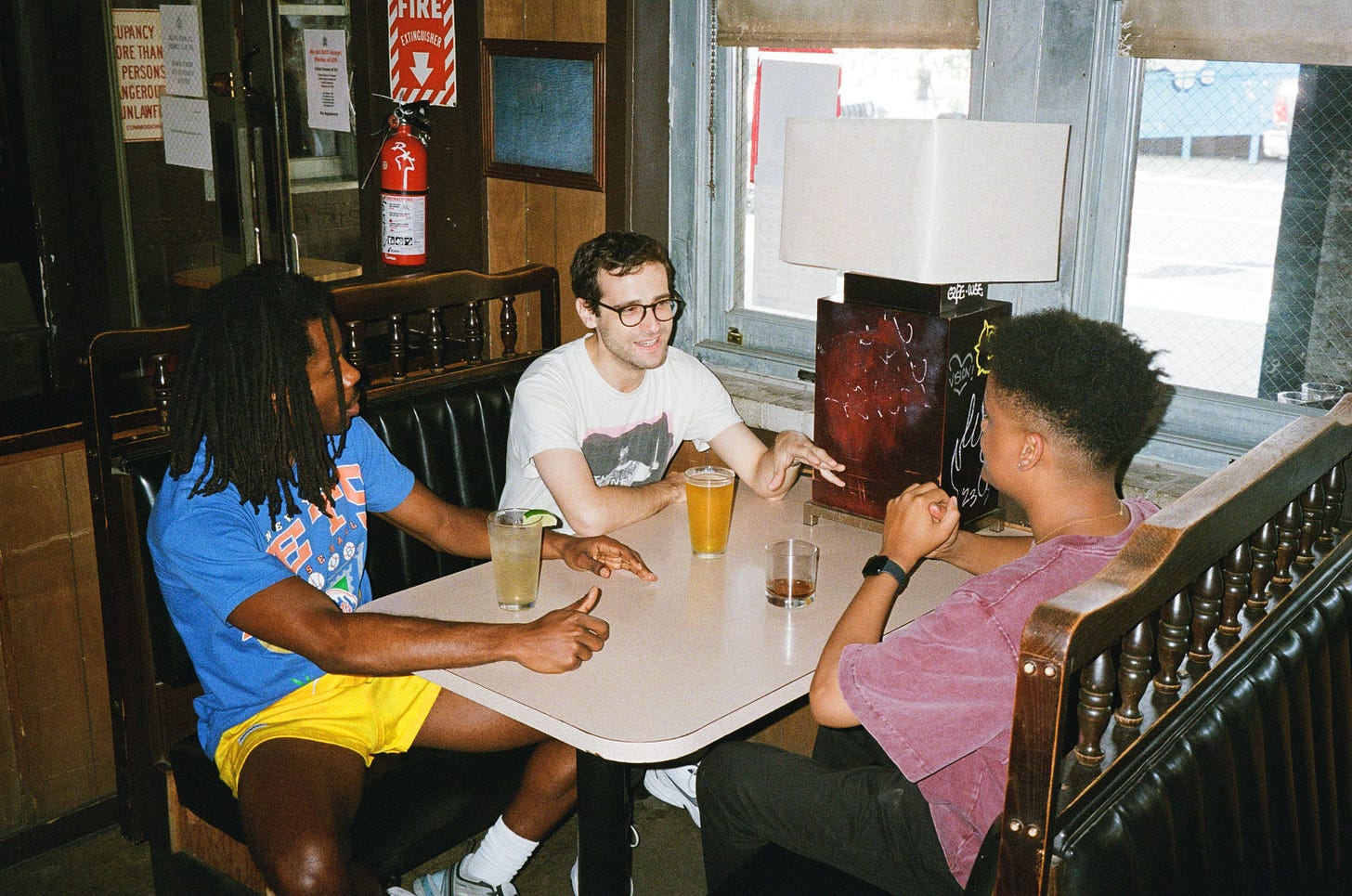 Manny, Noah, and Devan talking in a booth at a bar.