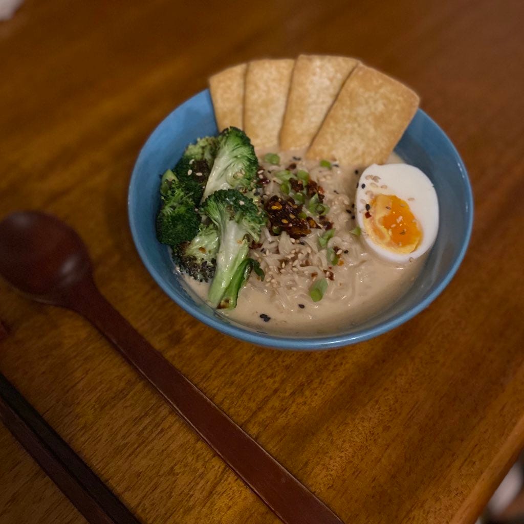 A blue bowl of the ramen described above, with tofu slices arrange on one side, plus broccoli, and half a boiled egg.