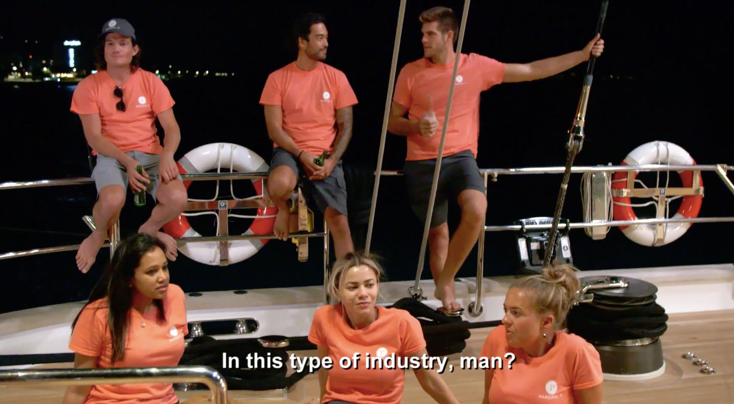 a group of six people in orange shirts sits on the deck of a yacht. someone is saying "in this type of industry, man?"