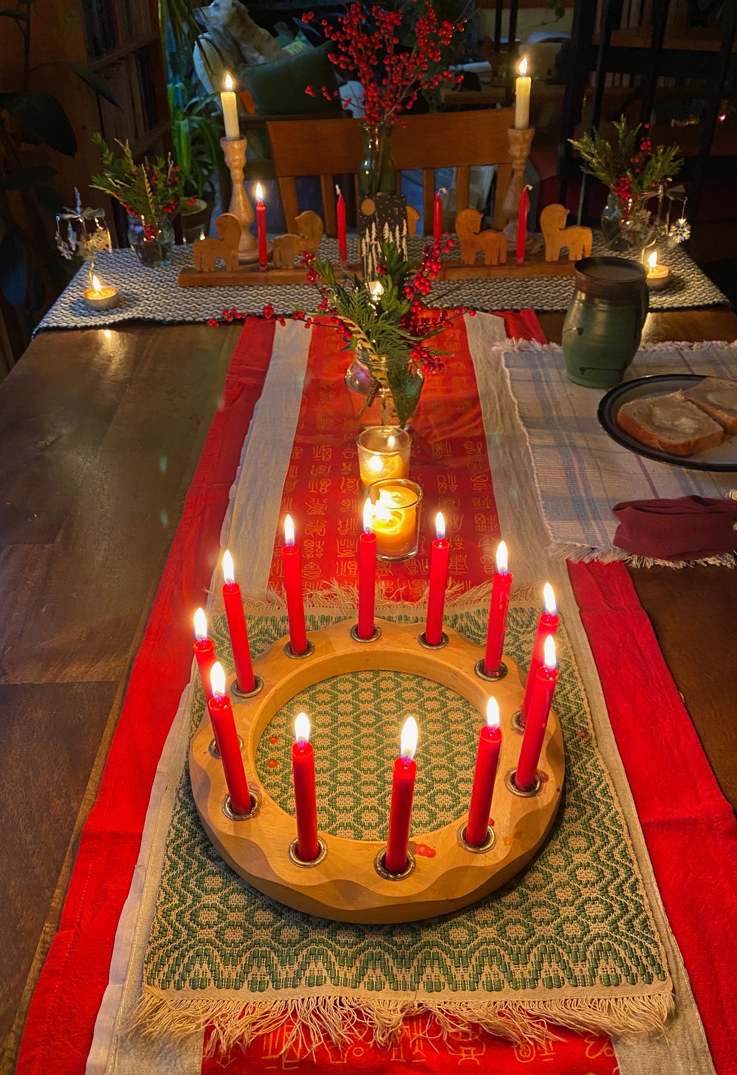A dining table with a bright red runner filled with lit candles of various sizes, and jars of winterberry and greenery.
