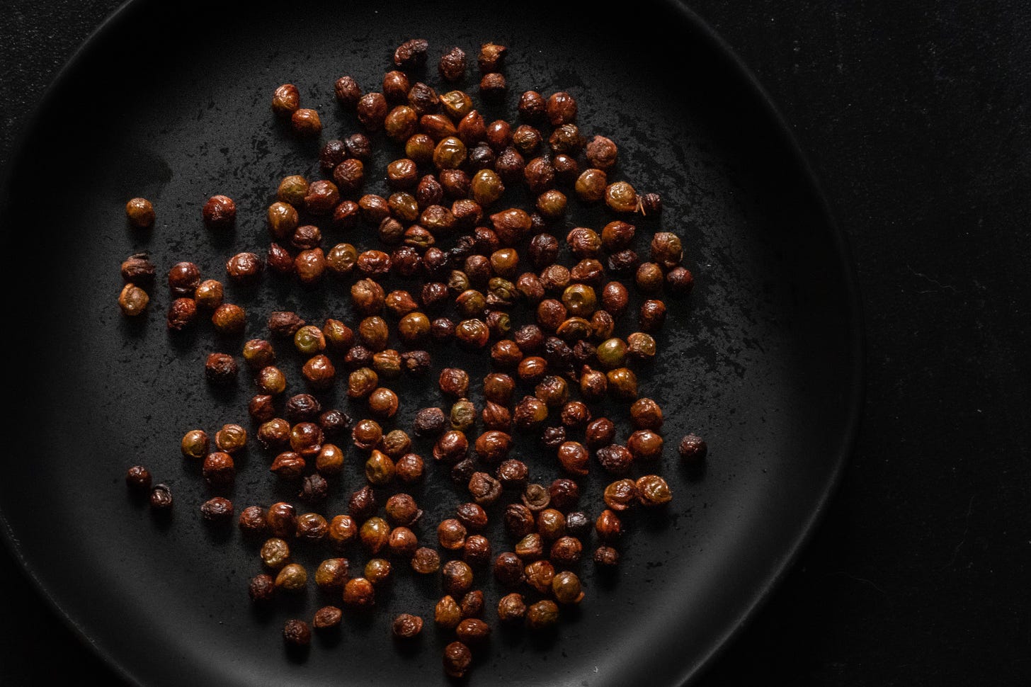 Dark photo of roasted maple seeds on a black plate with a black background, shot by JB Douglas for The Wild Grocery