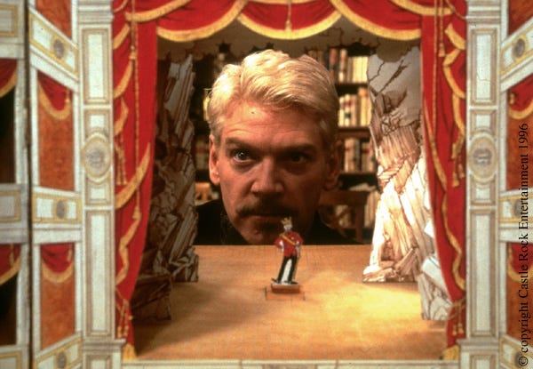 A screencap of Kenneth Branagh as Hamlet, staring from behind a diorama of a stage